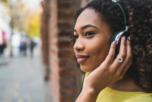 Portrait of young Afro american woman listening to music with headphones in the street. Outdoors. - 写真・画像