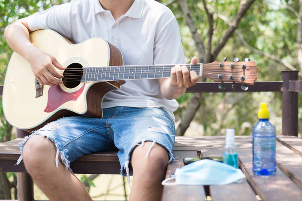 Músico tocando la guitarra acústica en el jardín en casa, Cuarentena durante el brote, Cerca de la mano derecha
. - Foto, Imagen