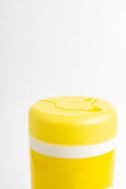 Um tiro macro de uma tampa superior amarela fechada de um recipiente de produto de toalhetes molhados desinfetante definido em fundo branco liso
. - Foto, Imagem