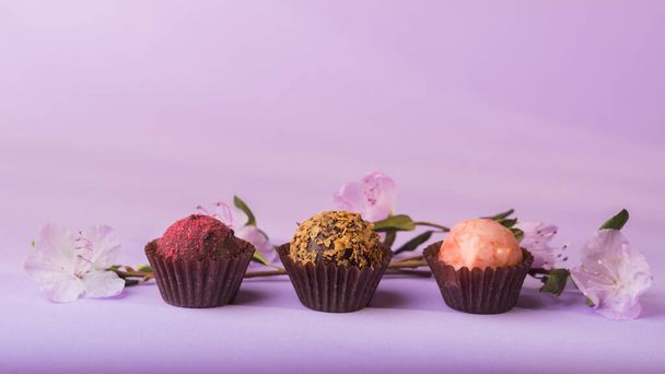 Une variété de bonbons au chocolat sur un fond violet décoré de fleurs fraîches
. - Photo, image