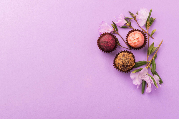 Een verscheidenheid aan chocolade snoepjes op een paarse achtergrond versierd met verse bloemen.Vlakke lay-out. - Foto, afbeelding