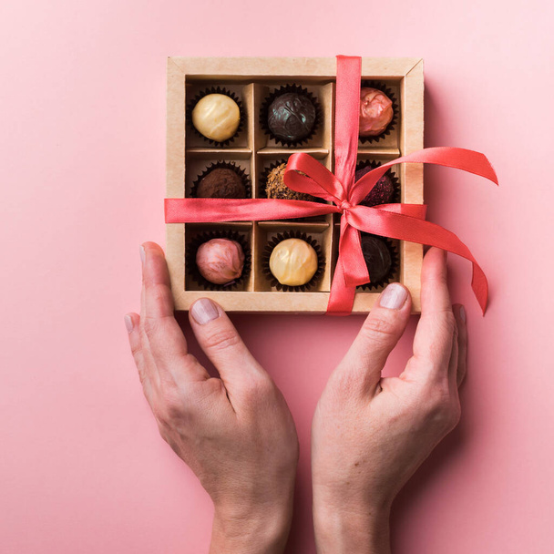 Nainen avaa rusetin ja avaa suklaarasian. Joukko erilaisia suklaata paperilaatikossa naisten käsissä
. - Valokuva, kuva