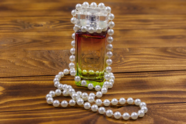 Bouteille de parfum et collier de perles sur fond bois
 - Photo, image