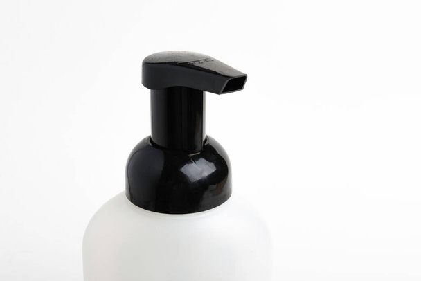 A close-up of the top portion of a black-and-white foaming hand soap dispenser set on a plain white background, - Photo, Image