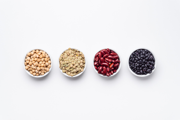Bean bowls top view white background. These legumes are all pulses (dry edible plant seeds). The following ingredients can be seen: chickpeas, red kidney beans, green lentils and black turtle beans. - Foto, Bild