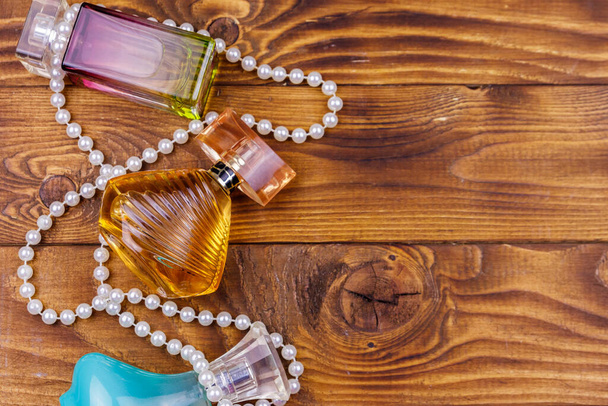 Différentes bouteilles de parfum et collier de perles sur fond en bois. Vue du dessus, espace de copie
 - Photo, image