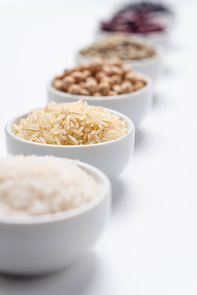 Basmati rizs hosszú gabona közelkép. Sekély mélységélesség a basmati rizsszemeken egy fehér tálban, más rizs gabonafélékkel és babhüvelyesekkel a háttérben. Függőleges irány. - Fotó, kép