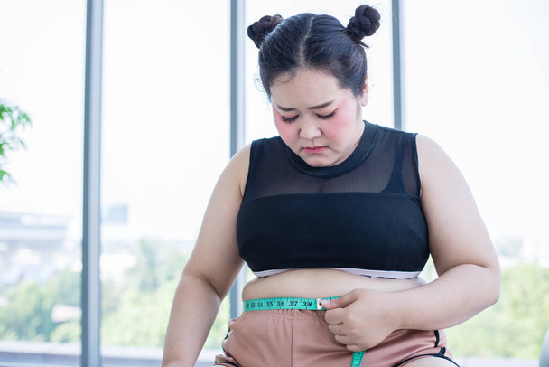 Mulher asiática com sobrepeso medindo camada de gordura com cintura em casa
 - Foto, Imagem