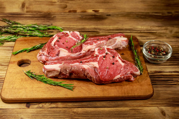 Kemiğin üstünde çiğ biftek, baharat ve ahşap masada biberiye. - Fotoğraf, Görsel