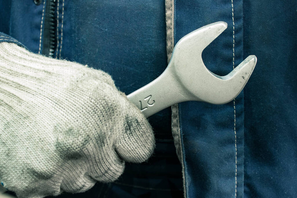 Trabajador con guantes sucios sostiene una llave inglesa. Hombre en ropa de trabajo con una llave inglesa
. - Foto, Imagen