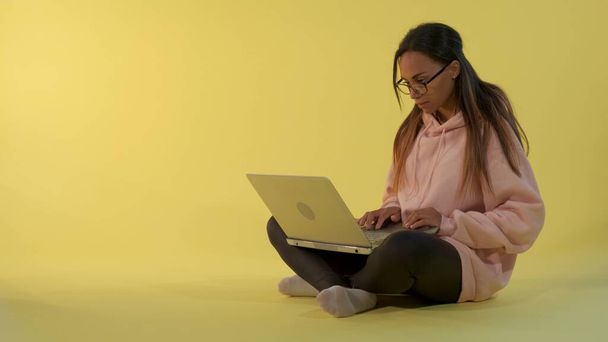 Inteligentna afrykańska dziewczyna pracuje na komputerze na żółtym tle - Zdjęcie, obraz