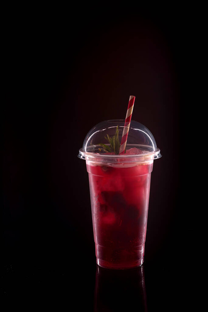 Refrescante limonada fresca con fresas, menta y hielo en vidrio de plástico con tapa sobre fondo negro
 - Foto, Imagen