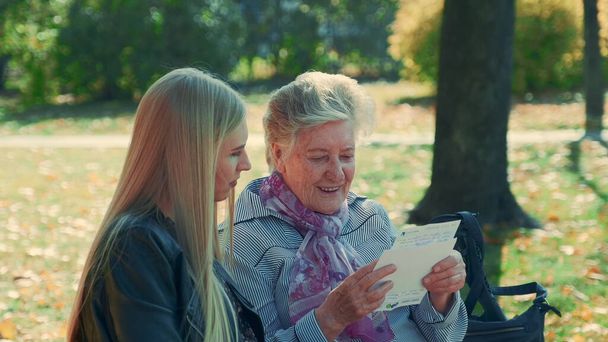 Střední zblízka staré ženy čtení dopis hezké mladé ženě v parku - Fotografie, Obrázek