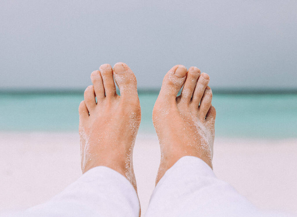 Mužské nohy na bílém písku u moře. Koncept cestování a dovolené - Fotografie, Obrázek