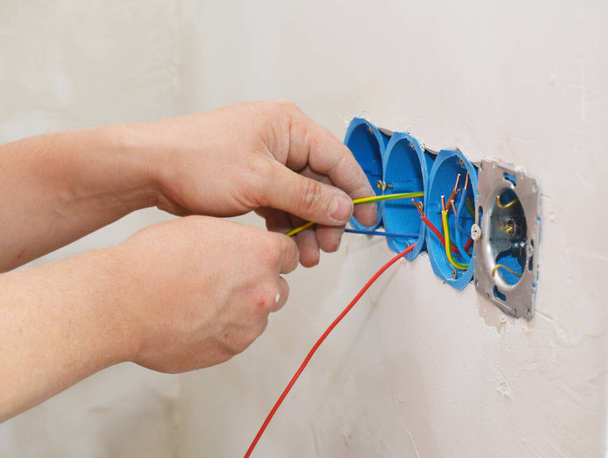 Un elettricista sta installando una nuova presa elettrica multipla installando i fili, cavo nella scatola di giunzione
. - Foto, immagini
