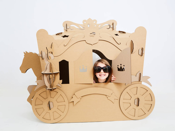 Little princess in crown 7 years old play in carriage made of brown cardboard - Fotoğraf, Görsel