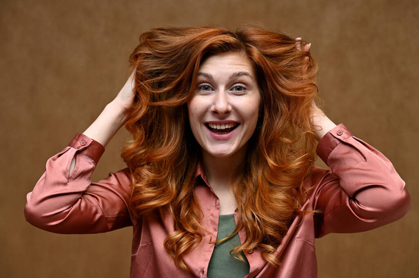 Portrait of actress caucasian woman with red hair showing joyful emotions. Photo taken in the studio on a beige background. The model is wearing a red shirt. - Φωτογραφία, εικόνα