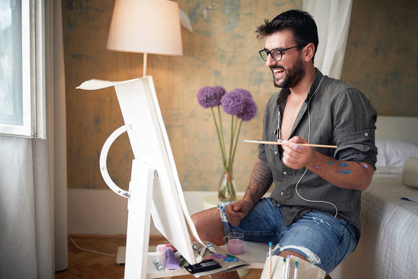 young male artist looking at his work, smiling, satisfied - Foto, Imagem