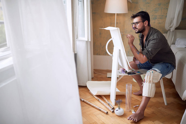 young male artist thoughtfully paint in a bedroom with white copy space - Photo, image