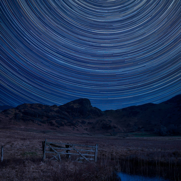 Digitales Kompositbild von Sternenpfaden rund um Polaris mit atemberaubendem Landschaftsbild von Blea Tarn im britischen Lake District bei Sonnenaufgang  - Foto, Bild
