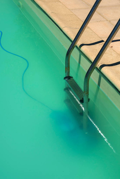 Manutenção da piscina - Um limpador automático de piscinas robô pode ser visto no fundo de uma piscina nublada, removendo detritos e algas
. - Foto, Imagem