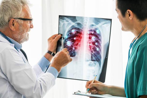 医師は、 X線フィルムに表示されているコロナウイルス病2019またはCovid-19を分析します。このフィルムは、コロナウイルスが肺および呼吸器に感染するシンボルを示しています。医療技術と医療の概念. - 写真・画像