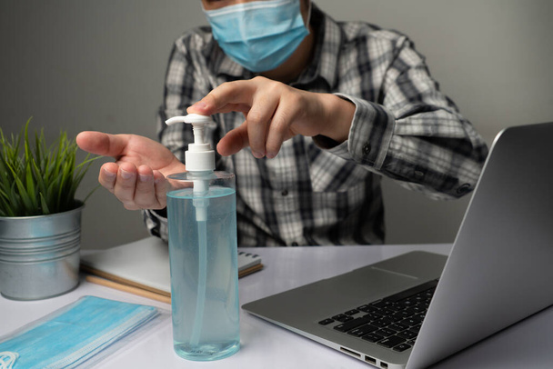 Coronavirus disease or COVID-19 protection concept - Young man work in office room at home with protective and cleaning equipment to protect against corona virus while using laptop computer at desk. - Фото, изображение