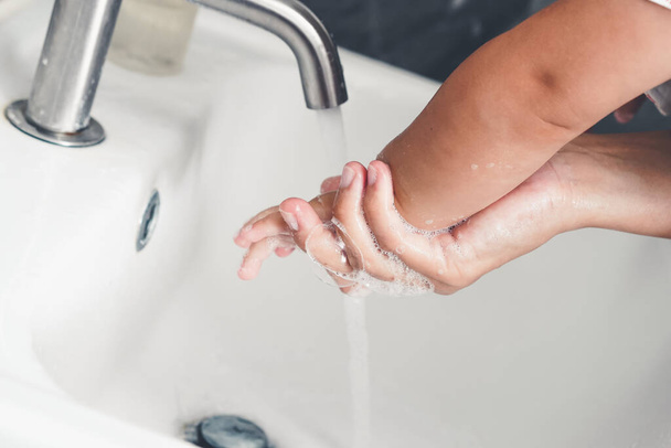 Matka myje rękę dziecka w celu zapobiegania nowatorskiej chorobie Coronavirus 2019 lub COVID-19. Ludzie myją ręce w umywalce, żeby oczyścić wirusa.. - Zdjęcie, obraz