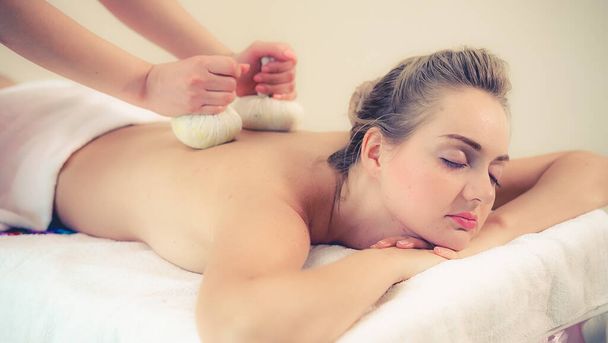 Θεραπευτής μασάζ κατέχει μια φυτική κομπρέσα για να κάνει θεραπεία σε γυναίκα ξαπλωμένη σε κρεβάτι spa σε ένα πολυτελές θέρετρο spa. Ευεξία, ανακούφιση από το στρες και αναζωογόνηση. - Φωτογραφία, εικόνα