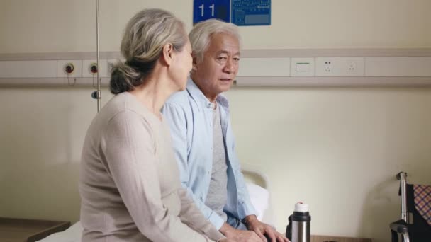 Senior asiatische Frau besucht und spricht mit depressivem Ehemann auf Krankenhausstation - Filmmaterial, Video