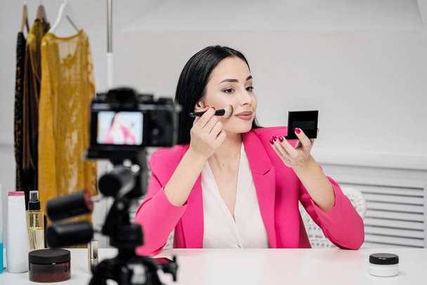 A beautiful young woman blogger in a pink jacket shoots a blog about cosmetics. - Zdjęcie, obraz