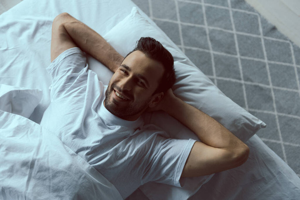 Fröhlicher junger Mann entspannt auf Kopfkissen zu Hause - Foto, Bild