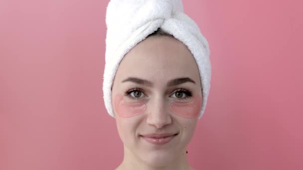 Plesant nude girl applying collagen eye masks on face in front of a mirror. Portrait of happy young woman smiling and posing in the studio for advertising. - Кадри, відео