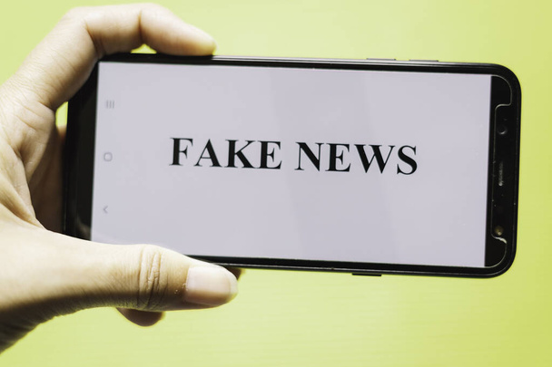 Hand holding smartphone with the phrase fake news written on the screen Conceptual of hoaxes and fake news through new technologies - Foto, Imagem