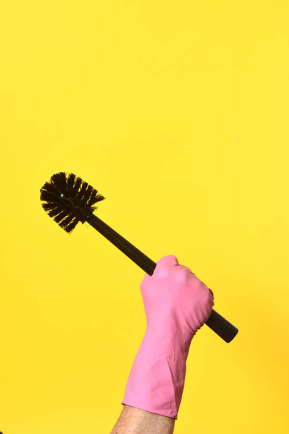 hand with glove hoding brush on yellow background - Foto, immagini