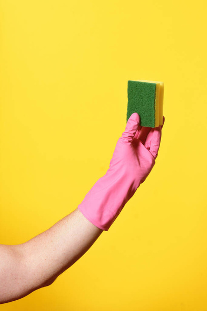 hand with glove hoding scourer on yellow background - Foto, imagen