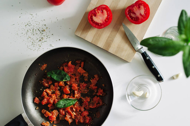 Вкусный итальянский томатный соус на черной сковороде с чесноком и листьями базилика вид сверху
 - Фото, изображение