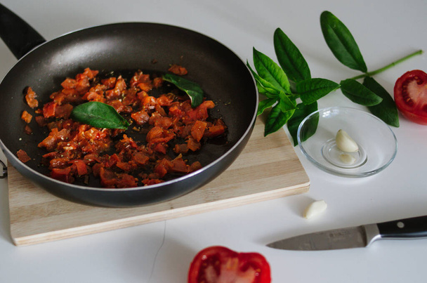 Вкусный итальянский томатный соус на черной сковороде с чесноком и листьями базилика
  - Фото, изображение