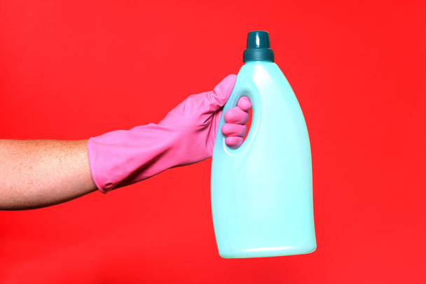 hand met handschoen en plastic fles zeep op rode achtergrond - Foto, afbeelding