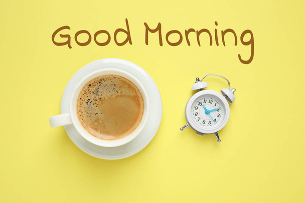 Cup of aromatic coffee and alarm clock on yellow background, flat lay. Good morning - Foto, Bild