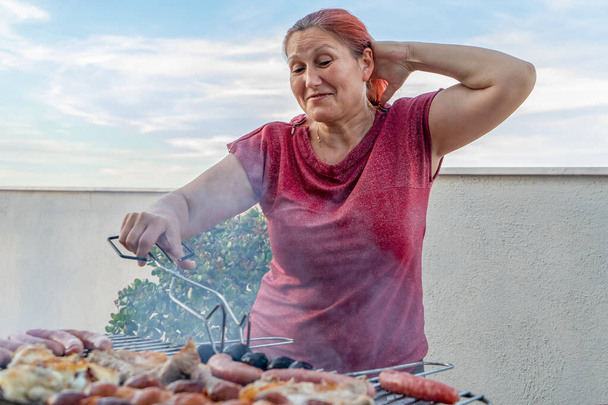 Donna rossa in camicia rossa con glitter fare barbecue sulla terrazza di casa sua
 - Foto, immagini