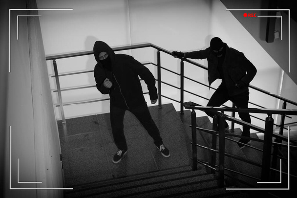 Criminals in masks on stairs indoors, view through CCTV camera - Foto, Imagen
