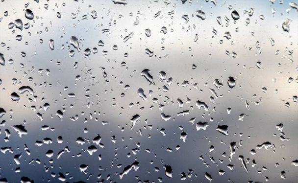 Gotas de lluvia en el vidrio, fondo del cielo azul con nubes de lluvia
. - Foto, imagen