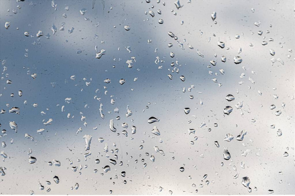 雨の雲と青い空の背景にガラスの上に雨滴. - 写真・画像