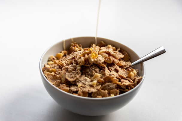 Desayuno saludable con miel dorada flotando sobre copos de maíz con nueces como deliciosa avena y dietas con una cuchara de plata para vegetarianos y orgánicos que sirven en la mañana ingredientes naturales
 - Foto, imagen