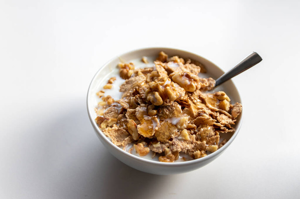 Gesundes Frühstück in einer weißen Schüssel mit goldenem Honig, der über Cornflakes mit Walnüssen und Milch schwebt, als leckeres Haferbrei mit Silberlöffel für Bio- und Vegetarier mit natürlichen Zutaten - Foto, Bild