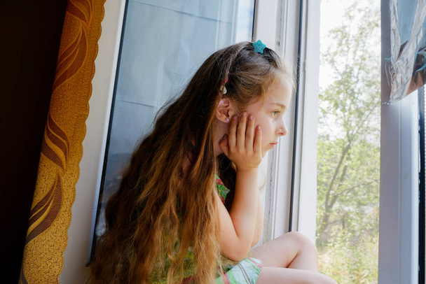 Kislány az ablaknál. Egy 5 éves kislány ül otthon az ablaknál. Gyerekkor, gyerek, ablak. Maradj otthon. - Fotó, kép