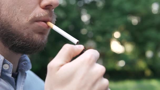 Mladý muž si zapálí cigaretu zblízka venku v parku - Záběry, video