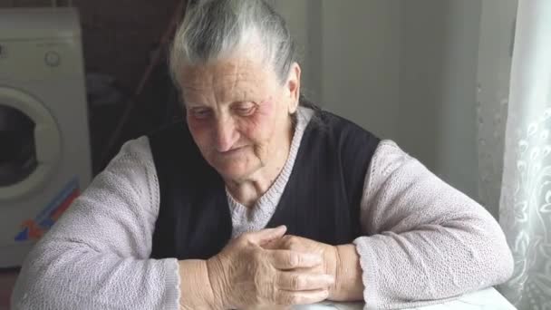 Yüzünde sivilceler olan yaşlı büyükanne masaya oturur ve hikayeyi anlatır. - Video, Çekim
