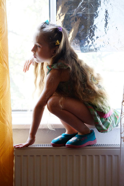 Little girl by the window. A 5 year old girl sits by the window at home. Childhood, child, window. Stay at home - Photo, Image